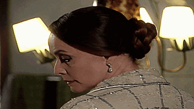 a woman wearing earrings and a bun looks down