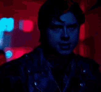 a man in a black leather jacket is standing in a dark room with red lights .