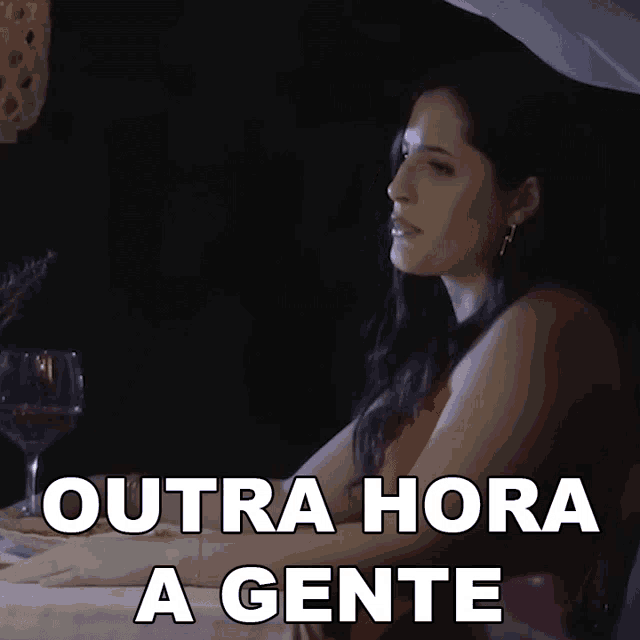 a woman sits at a table with outra hora a gente written on the bottom