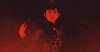 a girl in a red dress is standing in the dark .