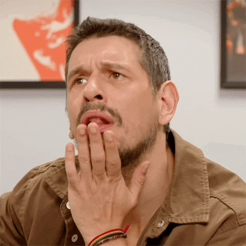 a man with a beard and a brown shirt is covering his mouth with his hands