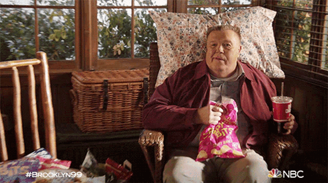 a man is sitting in a chair holding a bag of chips and a coke cup