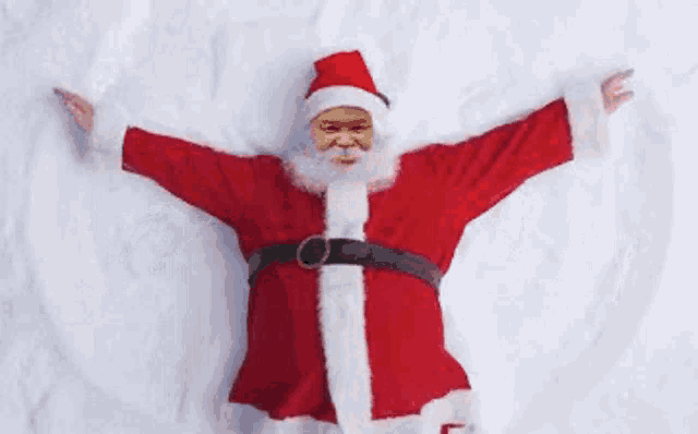 a man in a santa suit is laying in the snow .