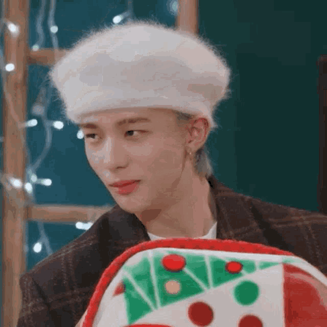 a young man wearing a white beret is sitting in front of a christmas present .
