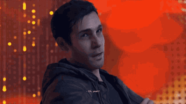 a man with his arms crossed looks at the camera with a red background behind him