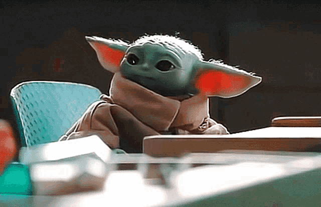 a baby yoda toy is sitting at a desk with a chair