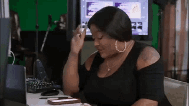 a woman in a black shirt is sitting at a desk with her hand on her head .