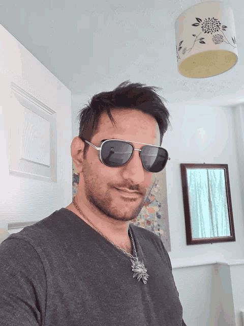 a man wearing sunglasses and a necklace stands in front of a mirror