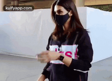 a woman wearing a black face mask and a black sweatshirt is standing in front of a white wall .
