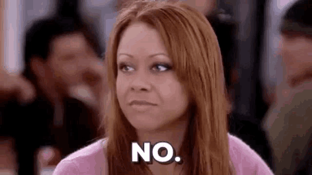 a woman in a pink shirt is sitting in a crowded room and saying no .