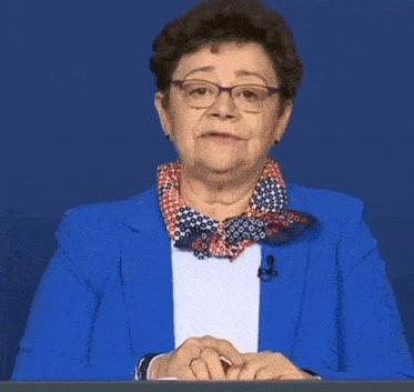 a woman wearing glasses and a blue jacket is sitting at a desk