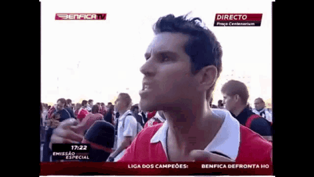 a man in a red shirt stands in front of a benfica tv advertisement