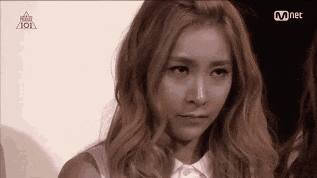 a girl with blonde hair is looking at the camera with a mnet logo in the background .