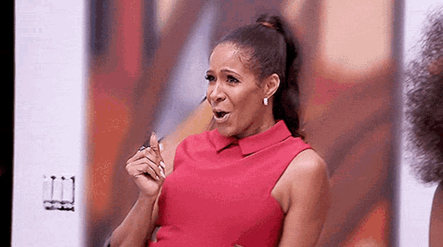 a woman in a red dress is sitting in front of a screen and making a funny face .