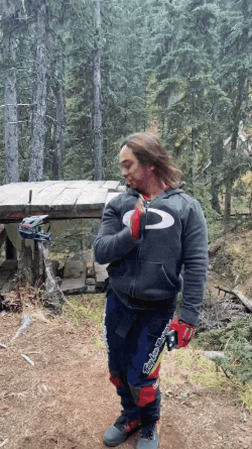 a man wearing a troy lee designs hoodie stands in a forest