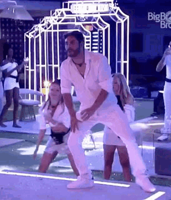 a man in a white shirt and white pants is dancing on a stage with two women .