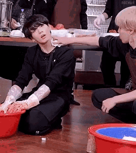 a man is kneeling on the floor while another man reaches for a bowl of meat .