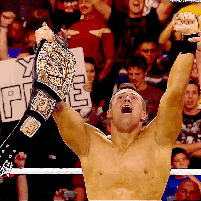 a shirtless wrestler is holding up his championship belt