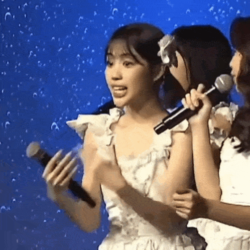 a woman in a white dress is holding a microphone while another woman holds a microphone .