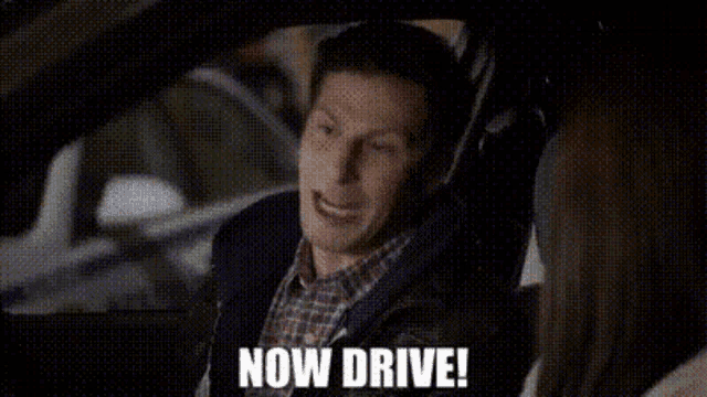 a man is sitting in the driver 's seat of a car and saying `` now drive '' .