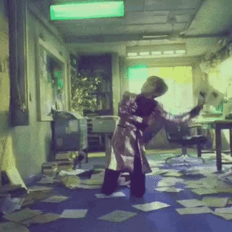 a person in a trench coat is dancing in a room with papers on the floor
