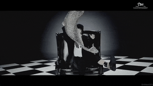 a woman in a fur coat sits in a chair with sm entertainment written on the bottom right