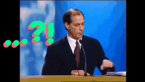 a man in a suit and tie speaking into a microphone with a question mark in the background