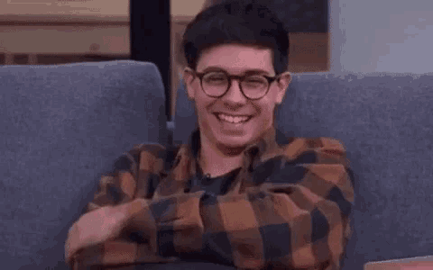 a young man wearing glasses is sitting on a couch smiling .