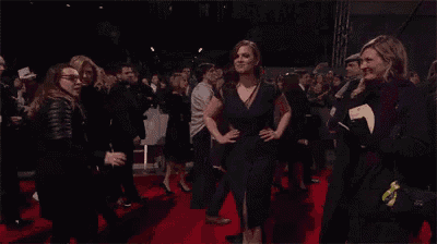 a woman in a black dress is walking on a red carpet surrounded by people