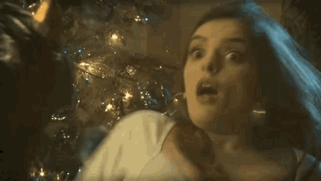 a woman with her mouth open is standing in front of a christmas tree