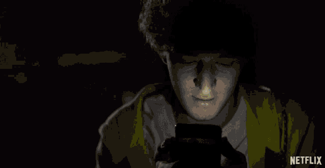 a man in a yellow jacket is looking at a cell phone with a netflix logo behind him