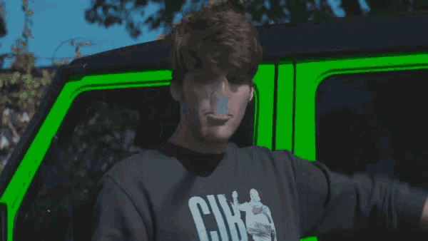 a man in a black shirt is standing in front of a green van .