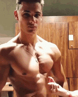 a shirtless man is flexing his muscles in a locker room while a woman holds his hand .