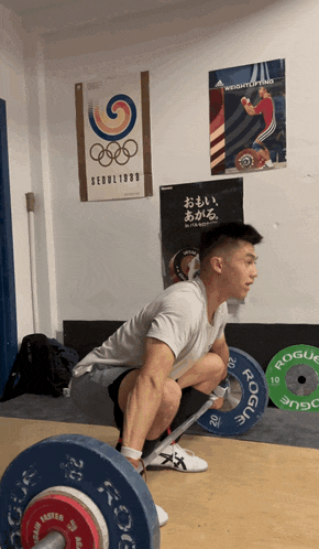 a man squatting down with a barbell in front of a poster that says weightlifting