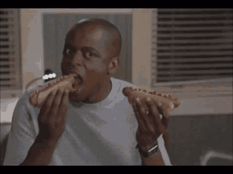 a man is eating a hot dog on a bun in a kitchen .
