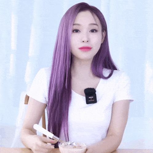 a woman with long purple hair is wearing a white shirt with a microphone on her neck