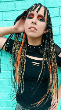 a woman with braids in her hair is standing in front of a blue brick wall