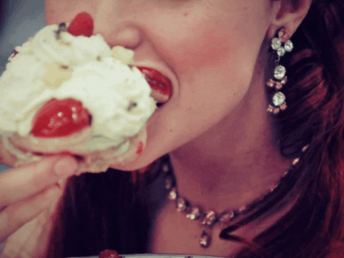 a woman is eating a cupcake with whipped cream and cherries on it