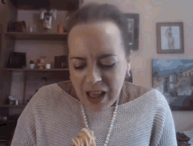 a woman wearing a grey sweater and pearls is eating a piece of food