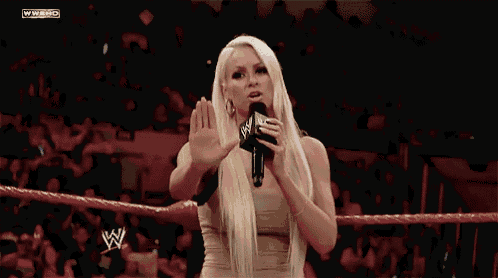 a woman stands in a wrestling ring holding a microphone with the letters wwe on the screen behind her