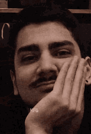 a man with a mustache is making a funny face with his hands on his face .
