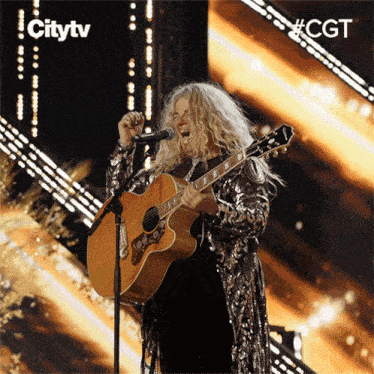 a woman is singing into a microphone while holding a guitar