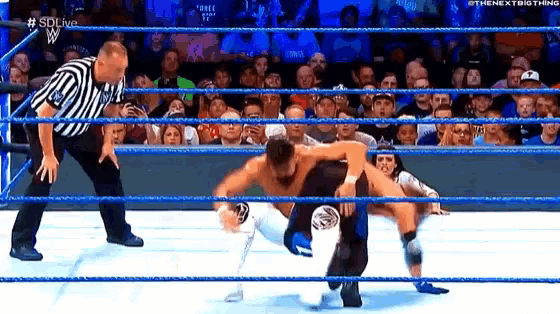 two men are wrestling in a wrestling ring while a referee stands behind them .