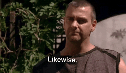 a man with a beard is standing in front of a tree with the words `` likewise '' written on the screen .