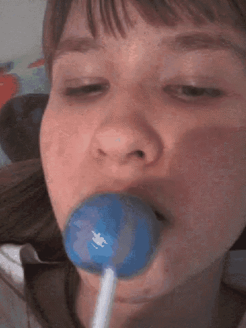 a girl is eating a blue lollipop in her mouth