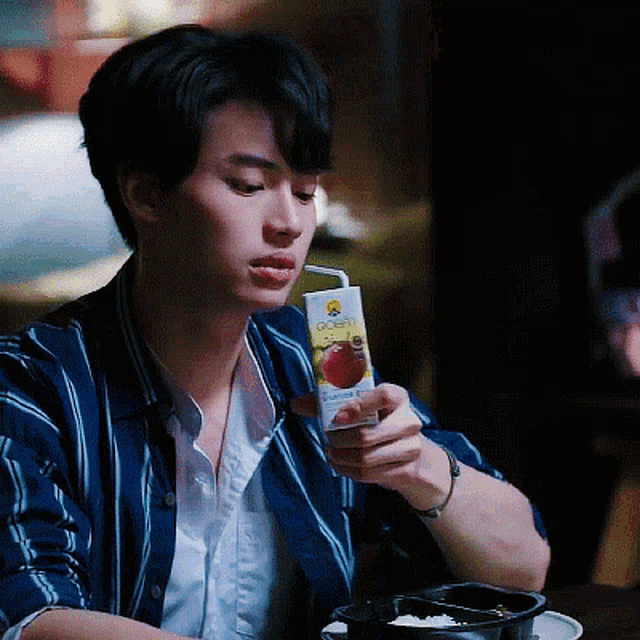 a man in a blue and white striped shirt is drinking a box of strawberry juice through a straw