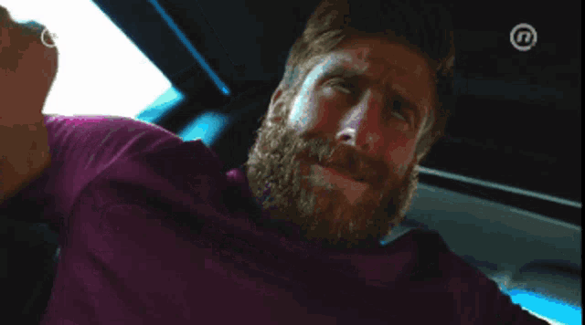 a man with a beard is sitting in a car with the number 13 on the bottom right corner