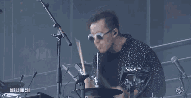 a man wearing sunglasses is playing drums in front of a microphone with the words rufos du sol below him