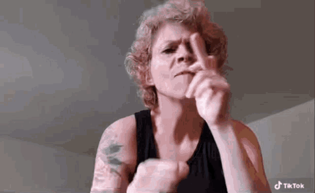 a woman in a black tank top is making a funny face with her finger .