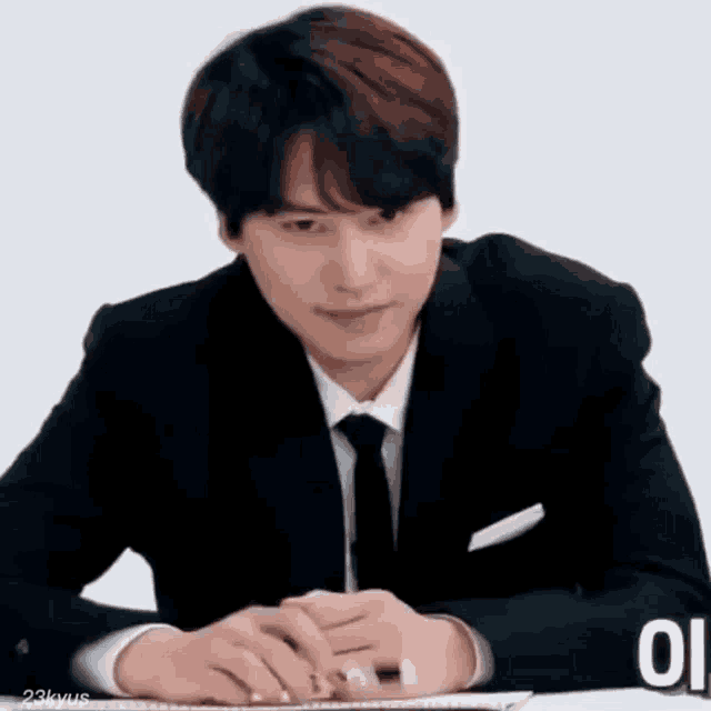 a man in a suit and tie is sitting at a desk with his hands folded .